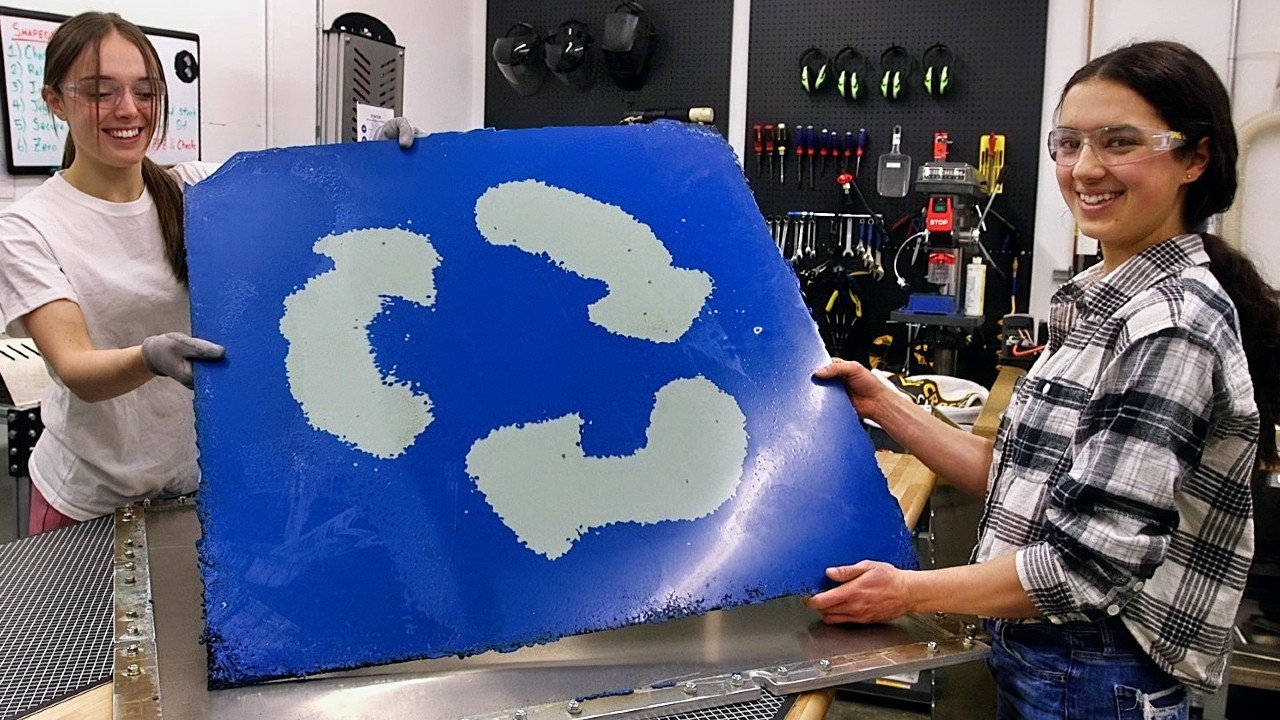 Two students holding up a large plastic blue square with white arrows in a lab.