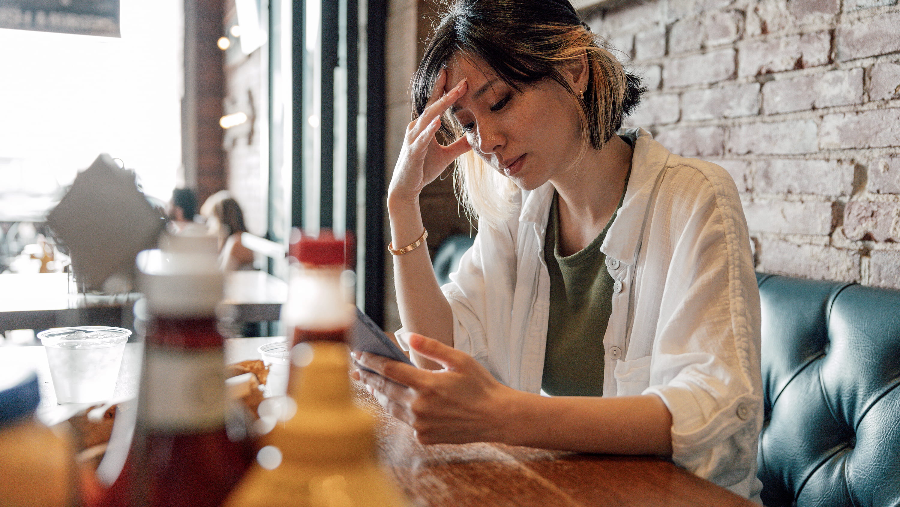 Pensive woman sits at a restaurant looking at her phone. (Photo: Getty Images)